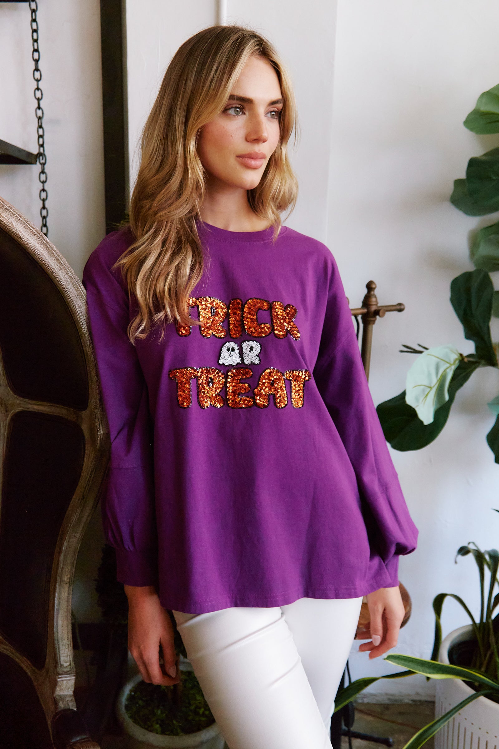 A woman wearing a Fantastic Fawn Purple Trick-or-Treat sequin sweatshirt.