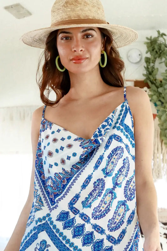 A woman wearing a Fantastic Fawn Sleeveless Bandana Print Woven Cowl Neck Camisole in Blue and white paisley dress and straw hat.