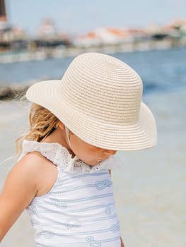 A little girl wearing a Sugar Bee Clothing girls sun hat on the beach.