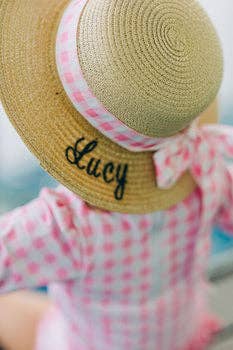 A little girl wearing a Sugar Bee Clothing Girls Sun Hat with the word lacy on it.