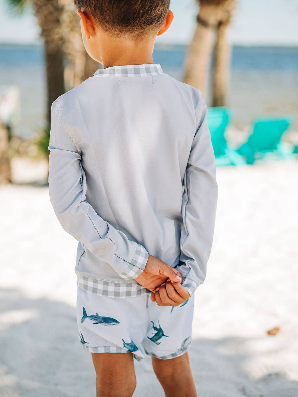 A little boy that is standing in the sand wearing Sugar Bee Clothing's Boys Gingham - Rashguard.