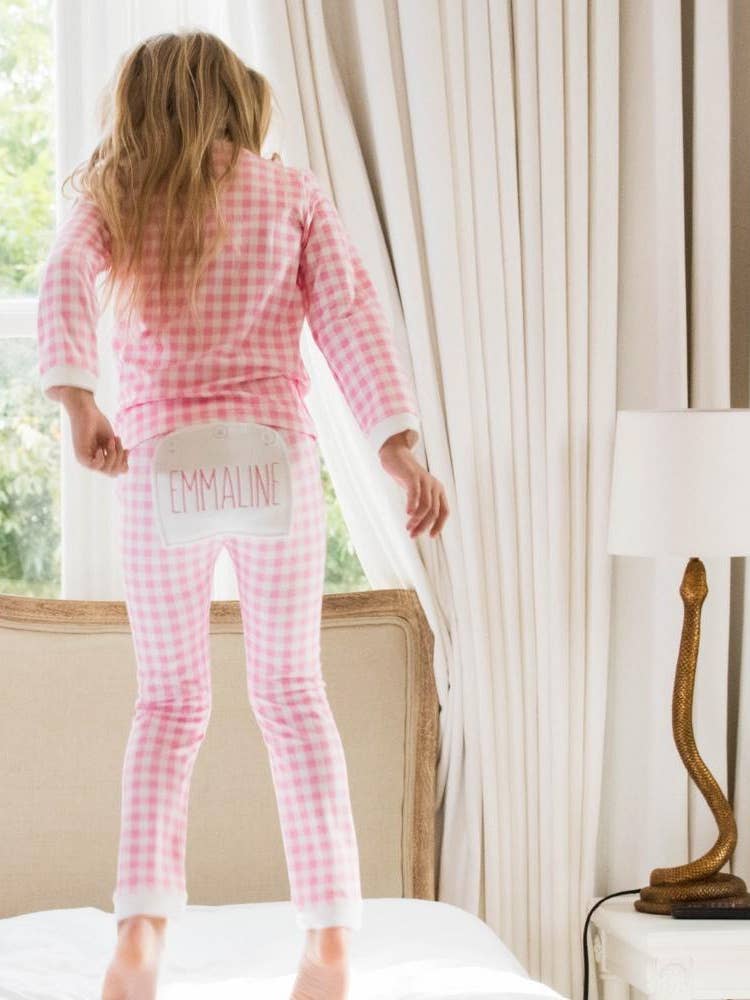 A woman in Sugar Bee Clothing's Pink Gingham Buttflap Pajamas is standing on a bed.