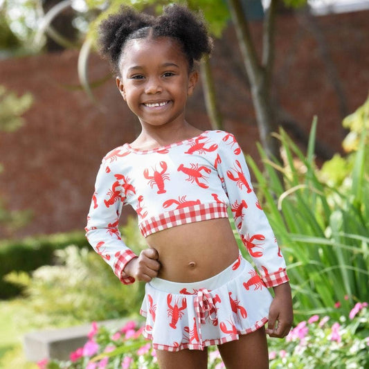 A little girl standing in front of a flower garden wearing the Crawfish Skirt Bikini by Sugar Bee Clothing.