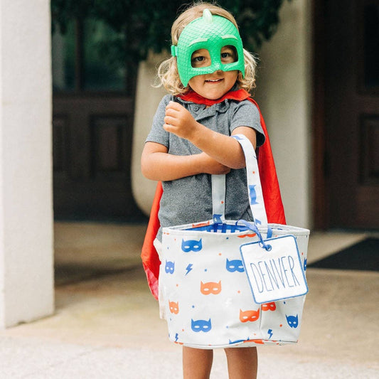 A little girl wearing a superhero mask holding a Halloween Basket - Superhero from Sugar Bee Clothing.