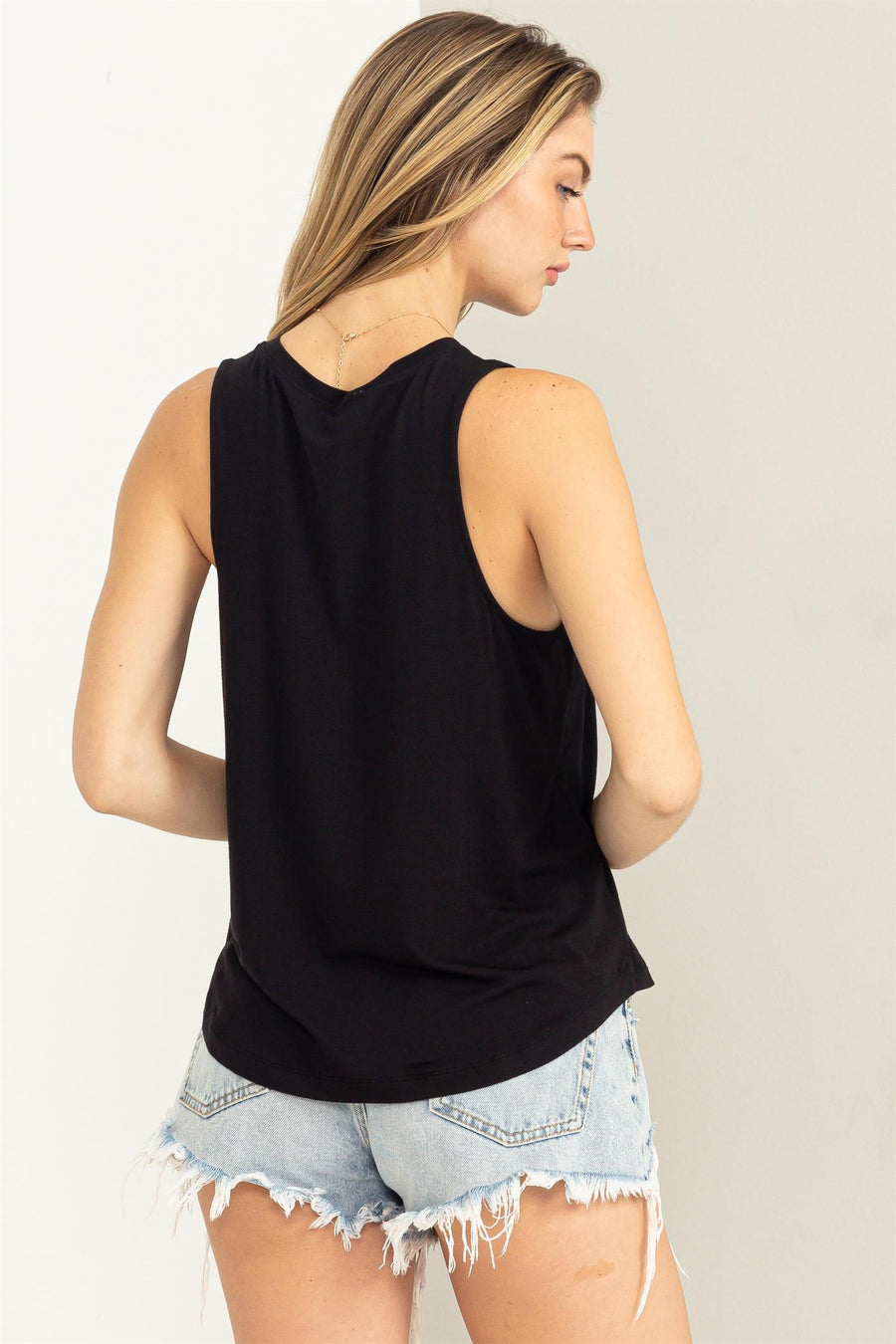 The back view of a woman wearing denim shorts and a HYFVE sleeveless black tank top.