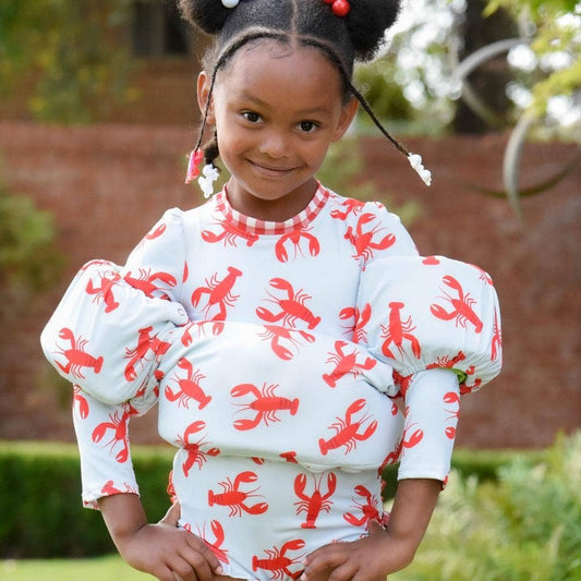 A young girl wearing a red and white Crawfish Floatie Cover dress by Sugar Bee Clothing.