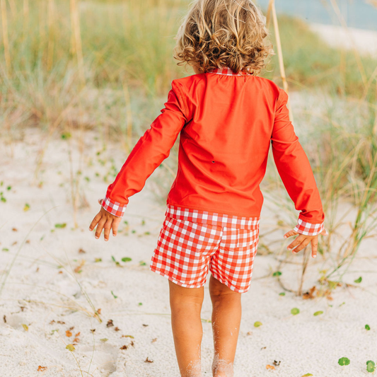 A little girl in a Sugar Bee Clothing Red Gingham Swim Shorts walking on the beach.