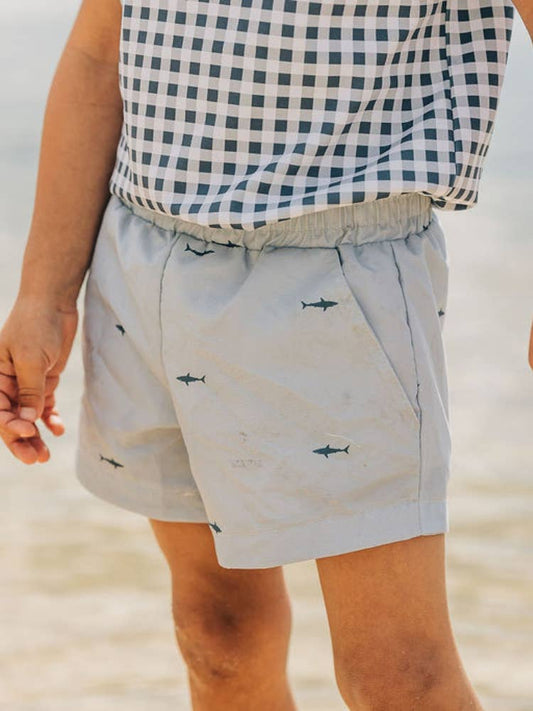 A close up of a person walking on the beach wearing Sugar Bee Clothing's Boys Shorts - Shark.