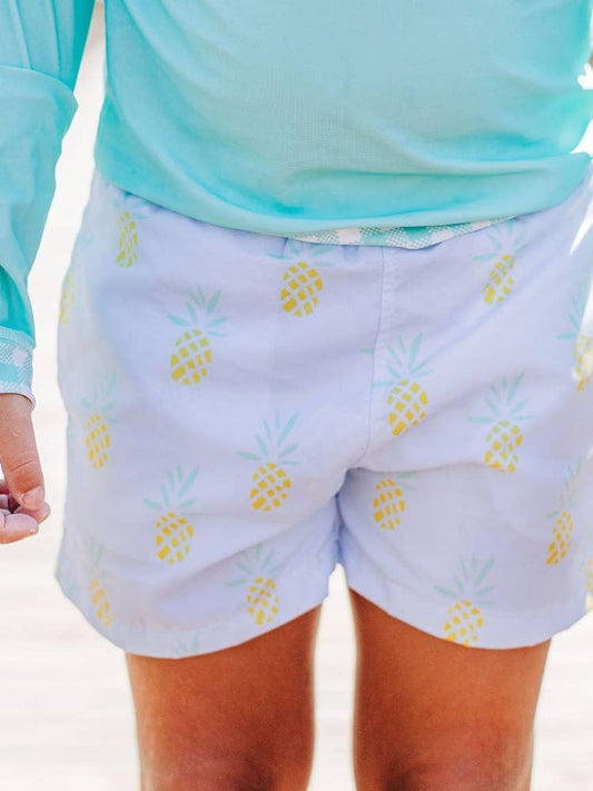 A person in Sugar Bee Clothing's Blue Pineapple Swim Shorts and a white shirt.