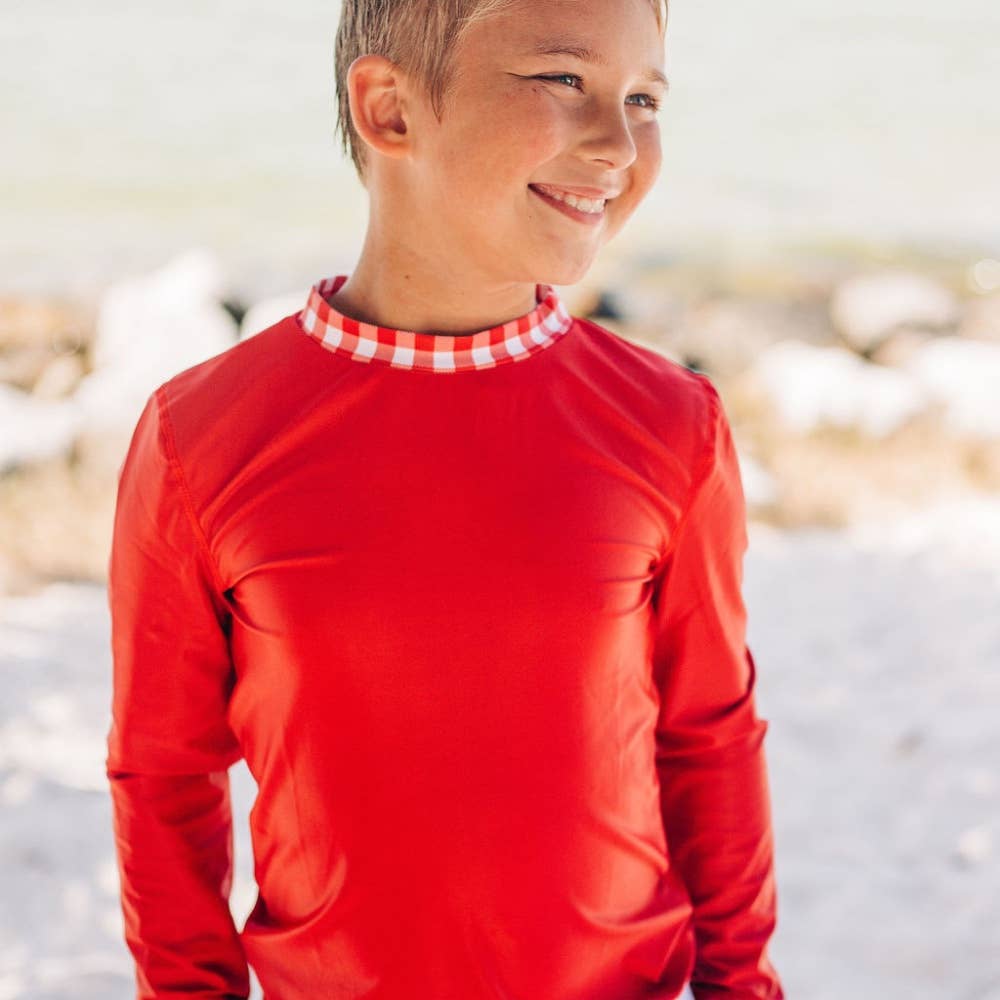 A young boy wearing a Sugar Bee Clothing Boys Gingham Rashguard.