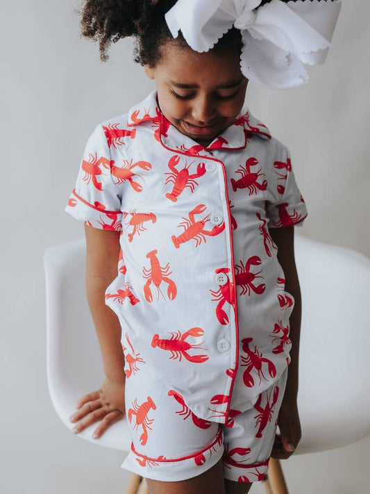 A little girl wearing Sugar Bee Clothing's red and white Crawfish Button Down Pajamas.