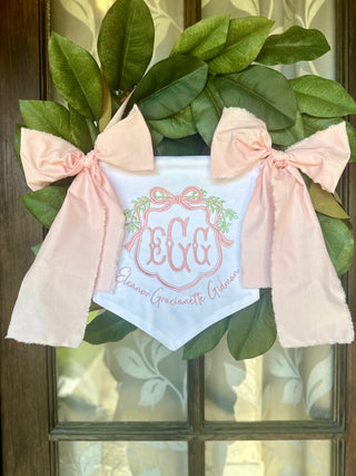 Decorative wreath with green leaves and pink bows on a glass door.