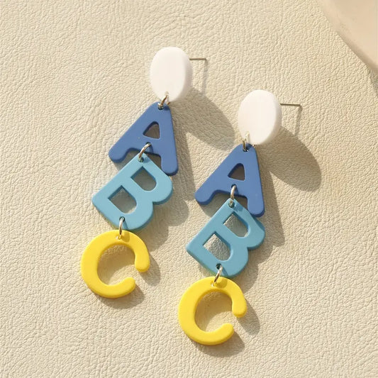 A pair of Chickie Collective ABC Clay Dangle Earrings with blue, yellow and white letters.