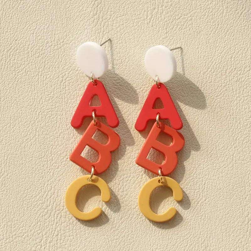 A pair of Chickie Collective ABC Clay Dangle Earrings with red, orange and yellow letters.