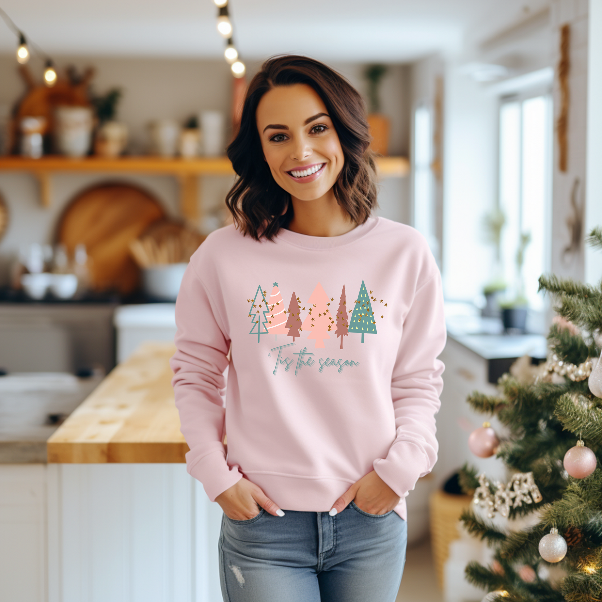 A cozy woman in a Light Pink Christmas Tree Sweatshirt from Printify poses in front of a Christmas tree.
