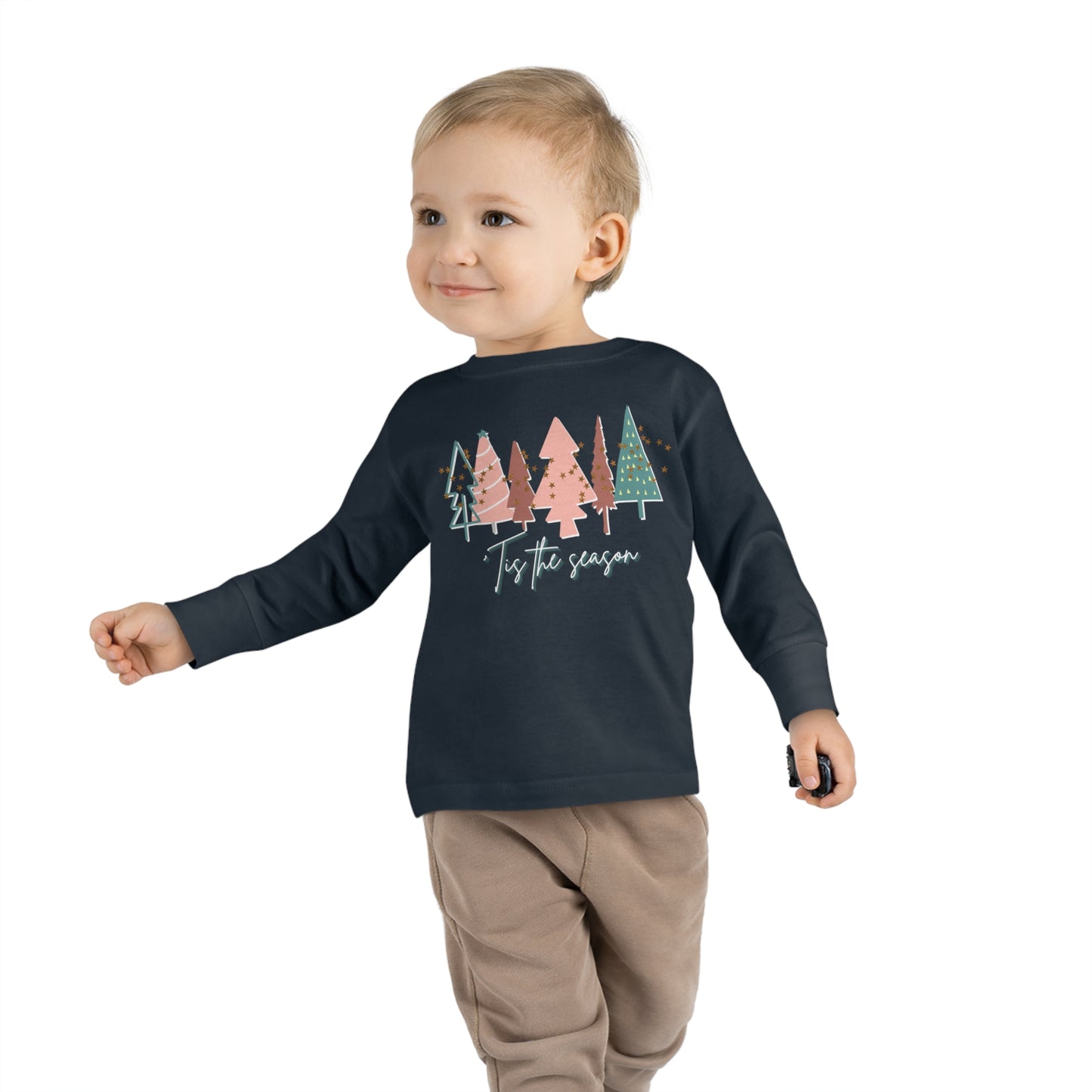 A young boy wearing a Kids Christmas Tree Long Sleeve Tee - Toddler Crew Neck T-Shirt purchased from an Printify Etsy store that specializes in toddler long sleeve Christmas tees, perfect for kids and parents.