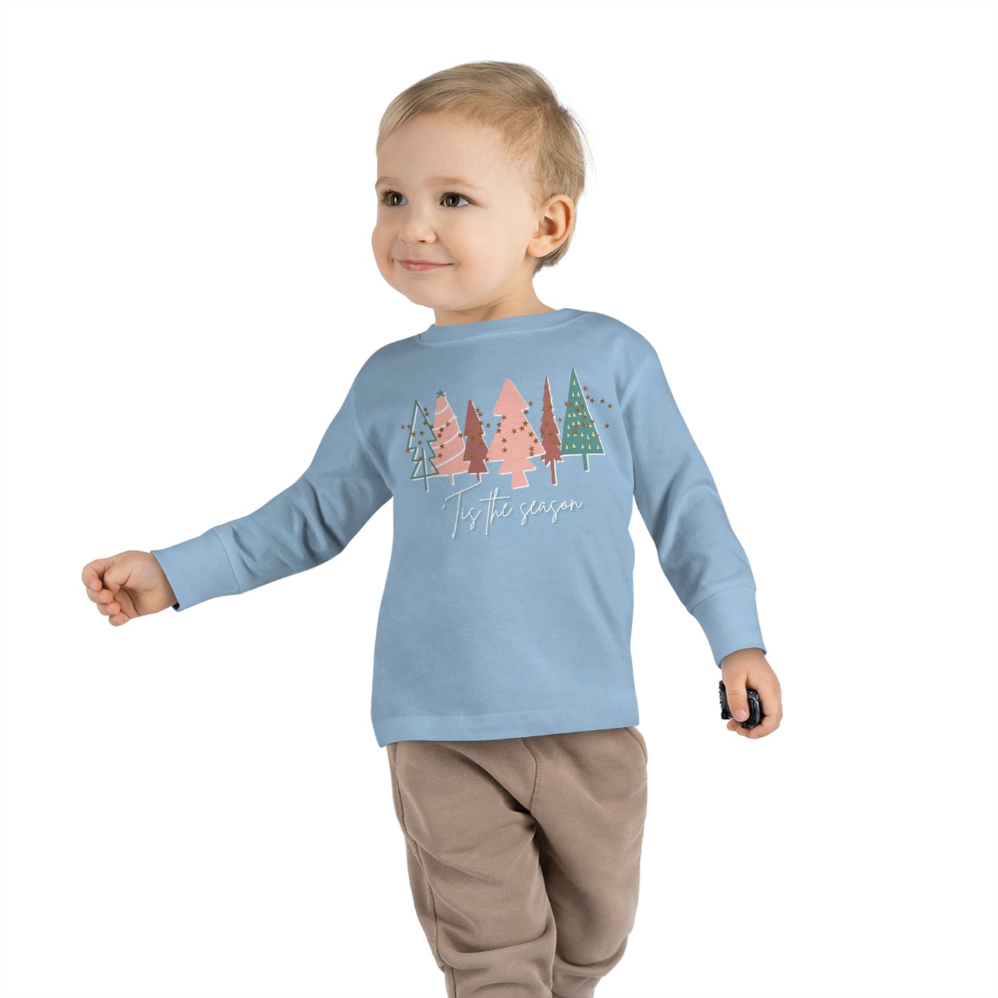 A toddler boy wearing a blue long-sleeve Kids Christmas Tree Long Sleeve Tee - Toddler Crew Neck T-Shirt by Printify with trees on it.
