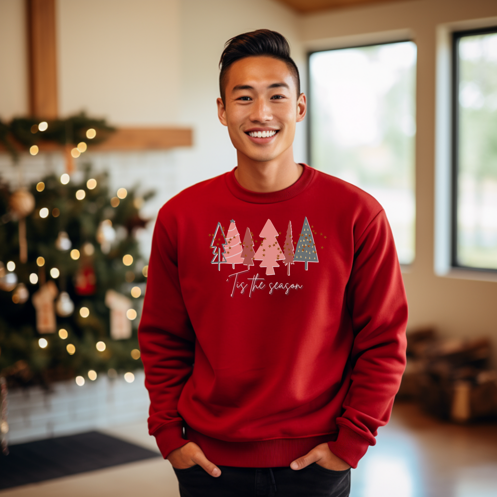 A man wearing a cozy Red Christmas Tree Sweatshirt by Printify in front of a Christmas tree.