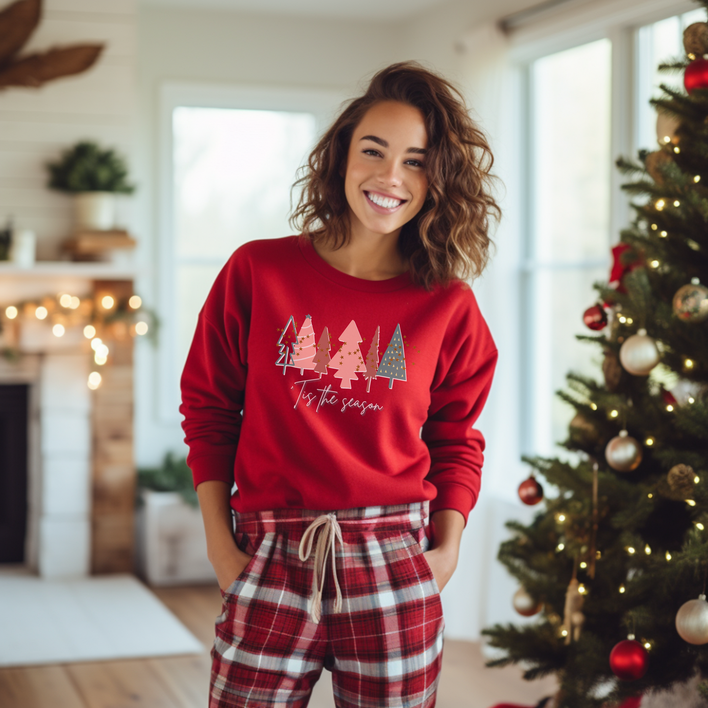 A woman wearing a Red Christmas Tree Sweatshirt by Printify in front of a Christmas tree.