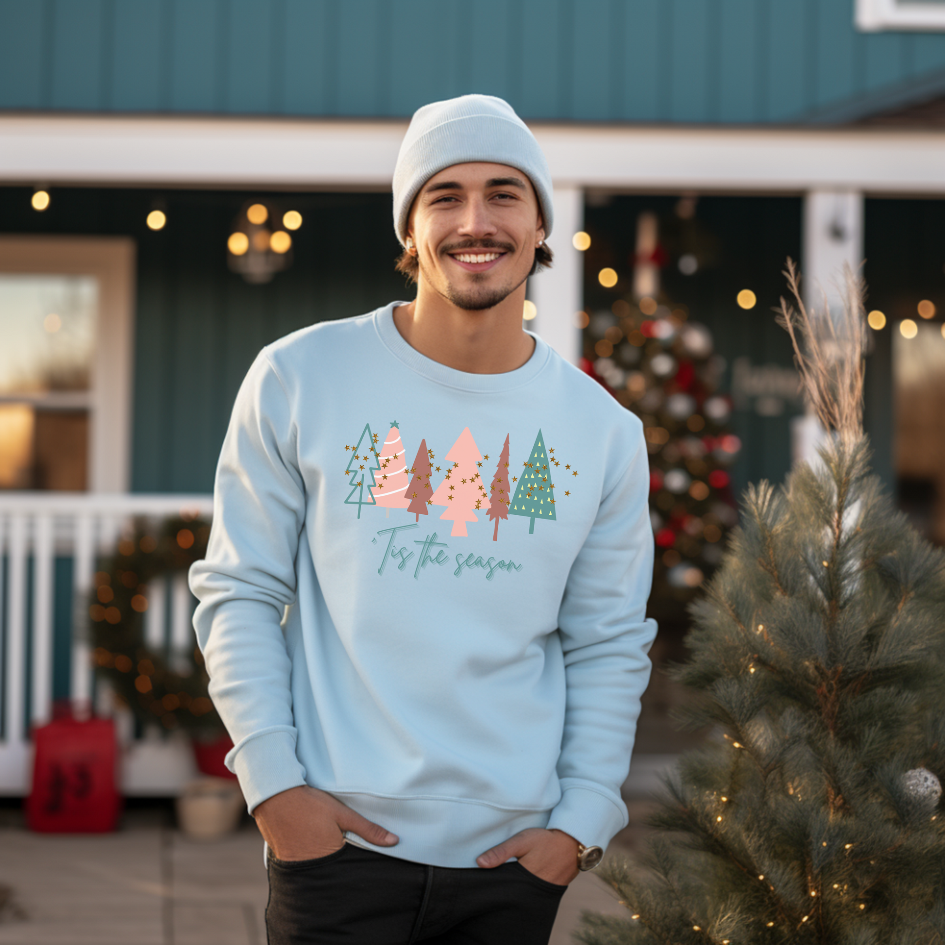 A man standing in front of a Christmas tree, warm and cozy in his Printify Light Blue Christmas Tree Sweatshirt.