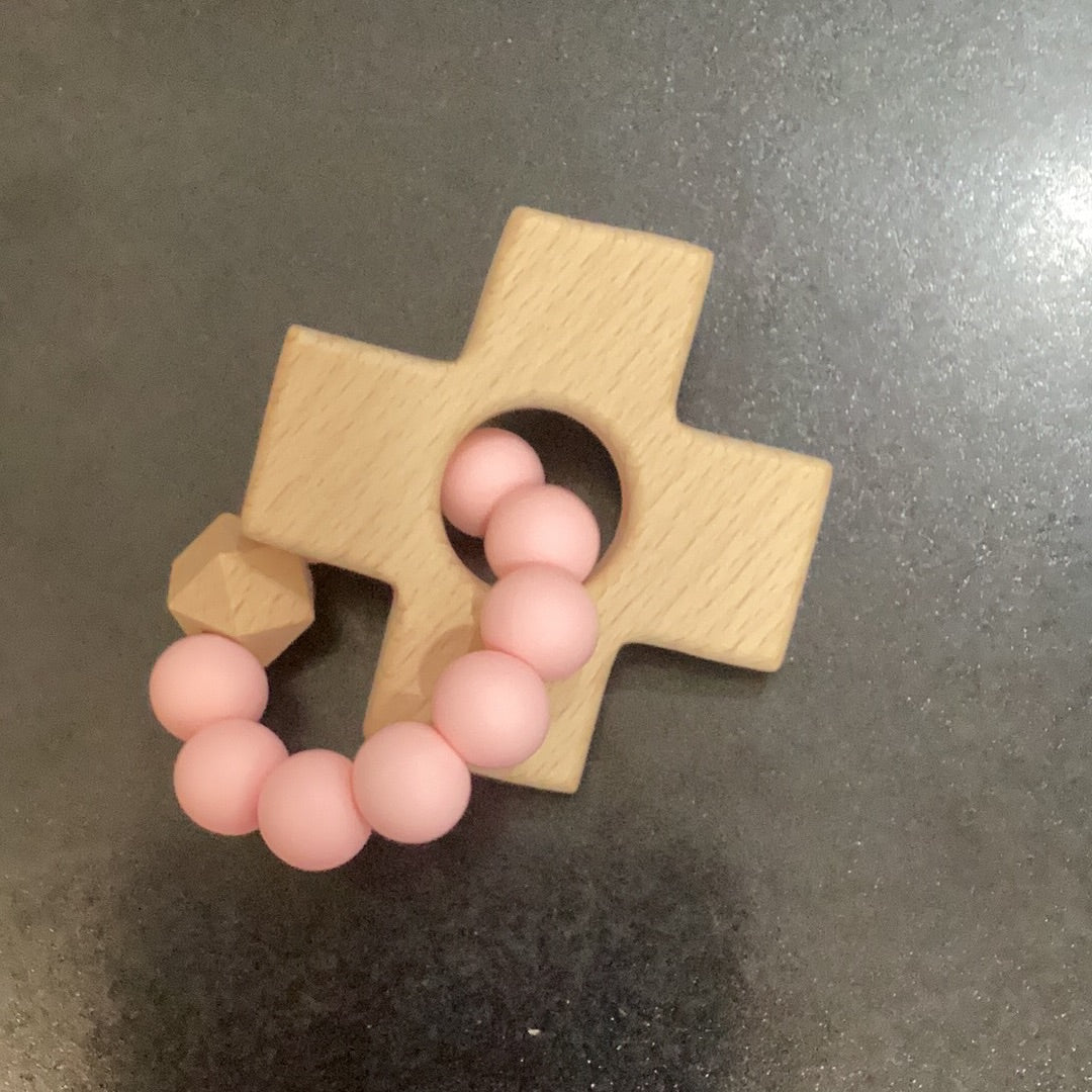 A Cross Teether with pink beads on it by Chickie Collective.