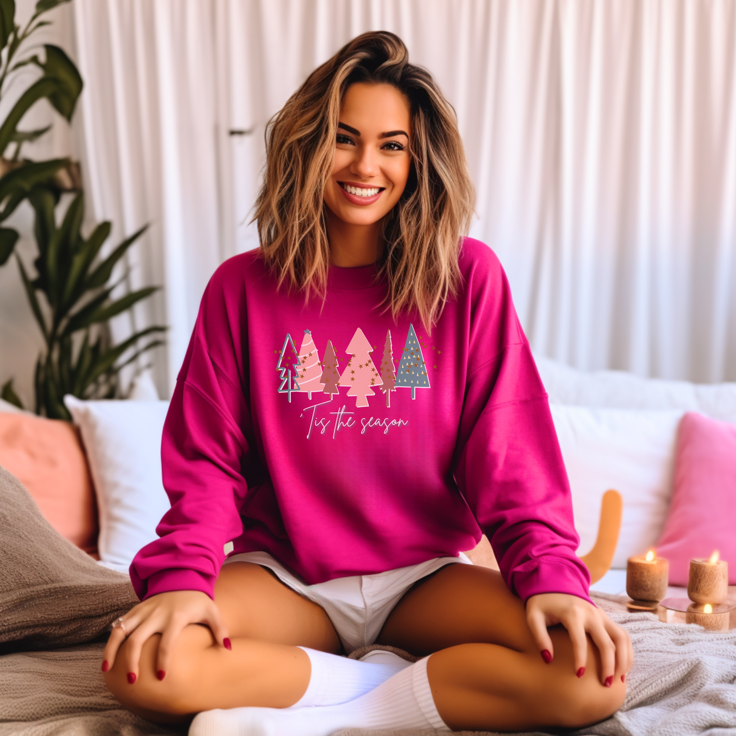 A cozy woman sitting on a bed wearing a Printify Bright Pink Christmas Tree Sweatshirt with trees on it, which is a crewneck sweatshirt and part of their ethical production line.