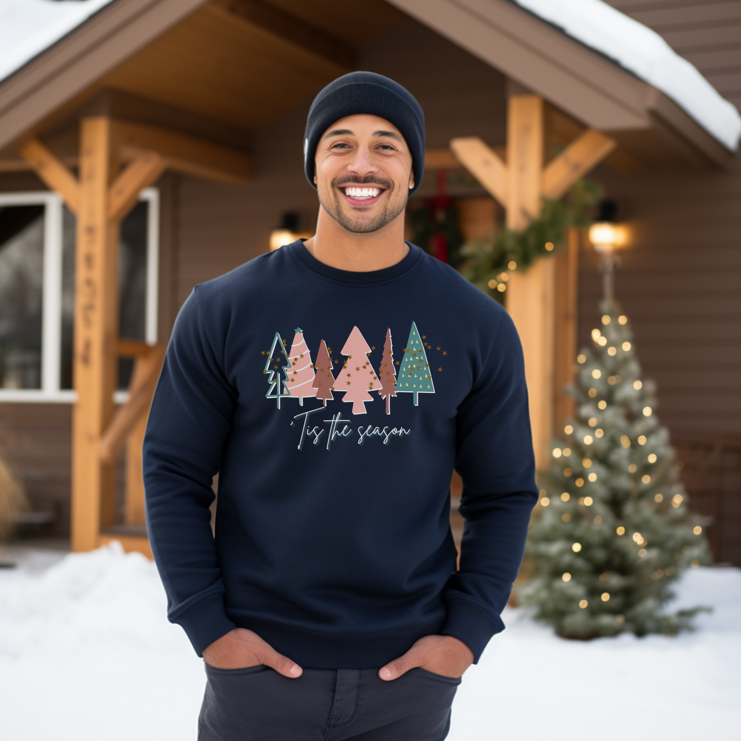 A cozy man wearing a Printify Navy Christmas Tree Sweatshirt in front of a house in the snow.