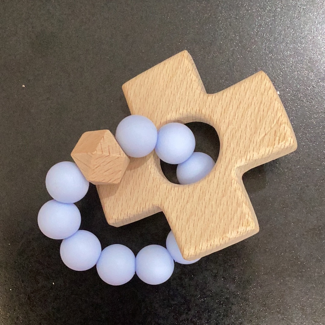 A Cross Teether by Chickie Collective with blue beads on it.