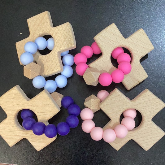 A set of Chickie Collective Cross Teethers with pink, purple, and blue beads.