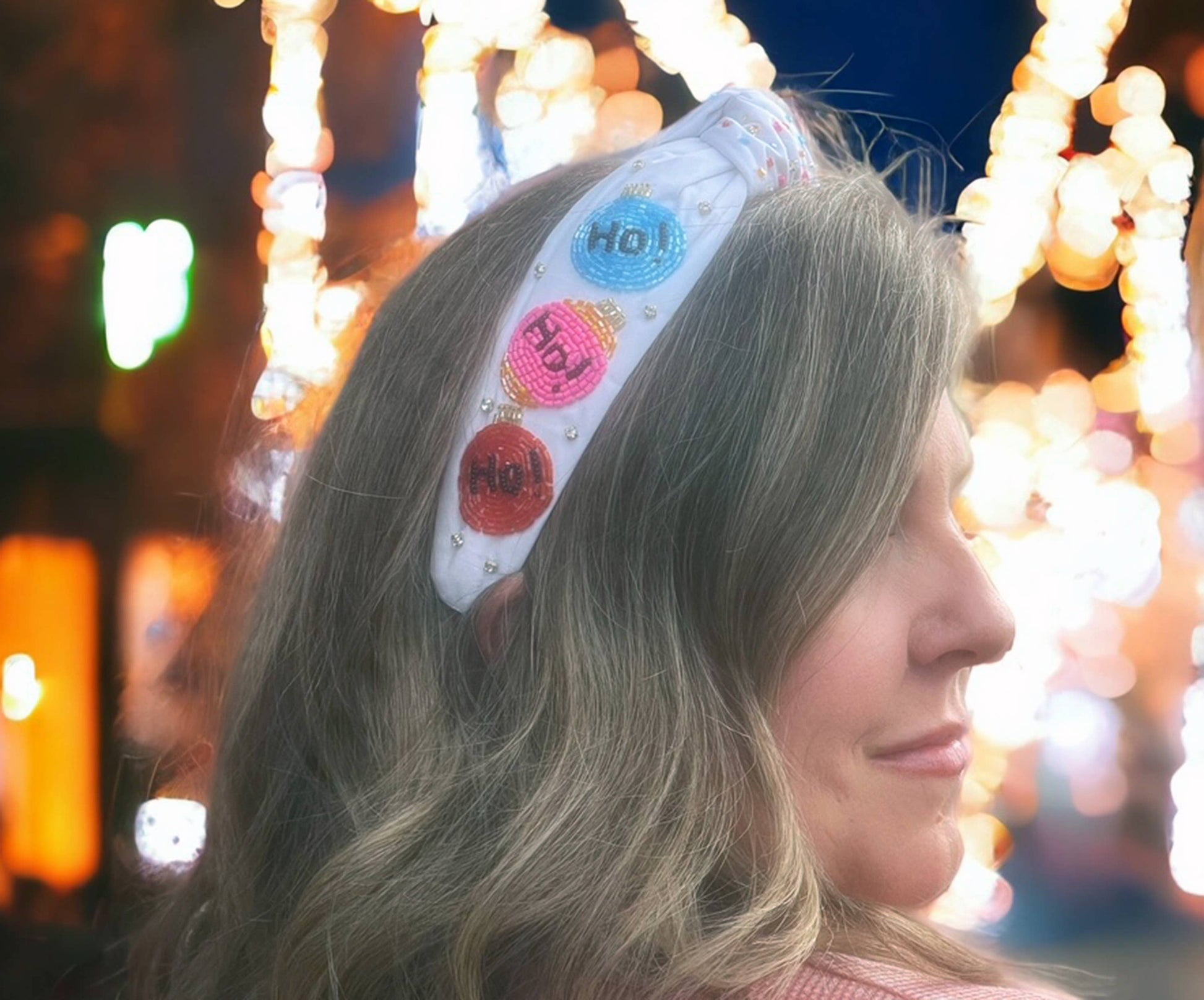 A woman wearing a Beaded Pink Christmas Lights Headband - Festive Holiday Accessories by Bash.