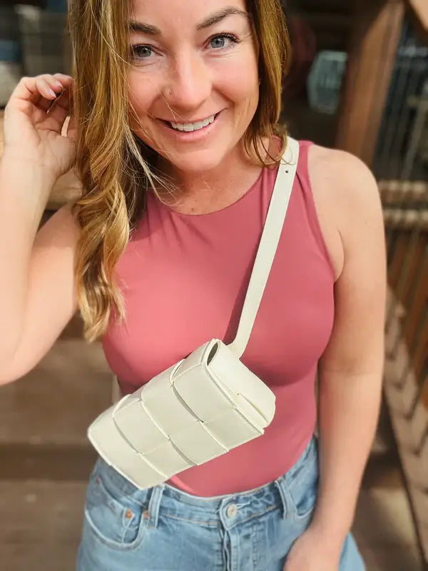 a woman wearing a pink tank top and jeans holding a Kaydee Lynn Kelsey Belt Bag - White.