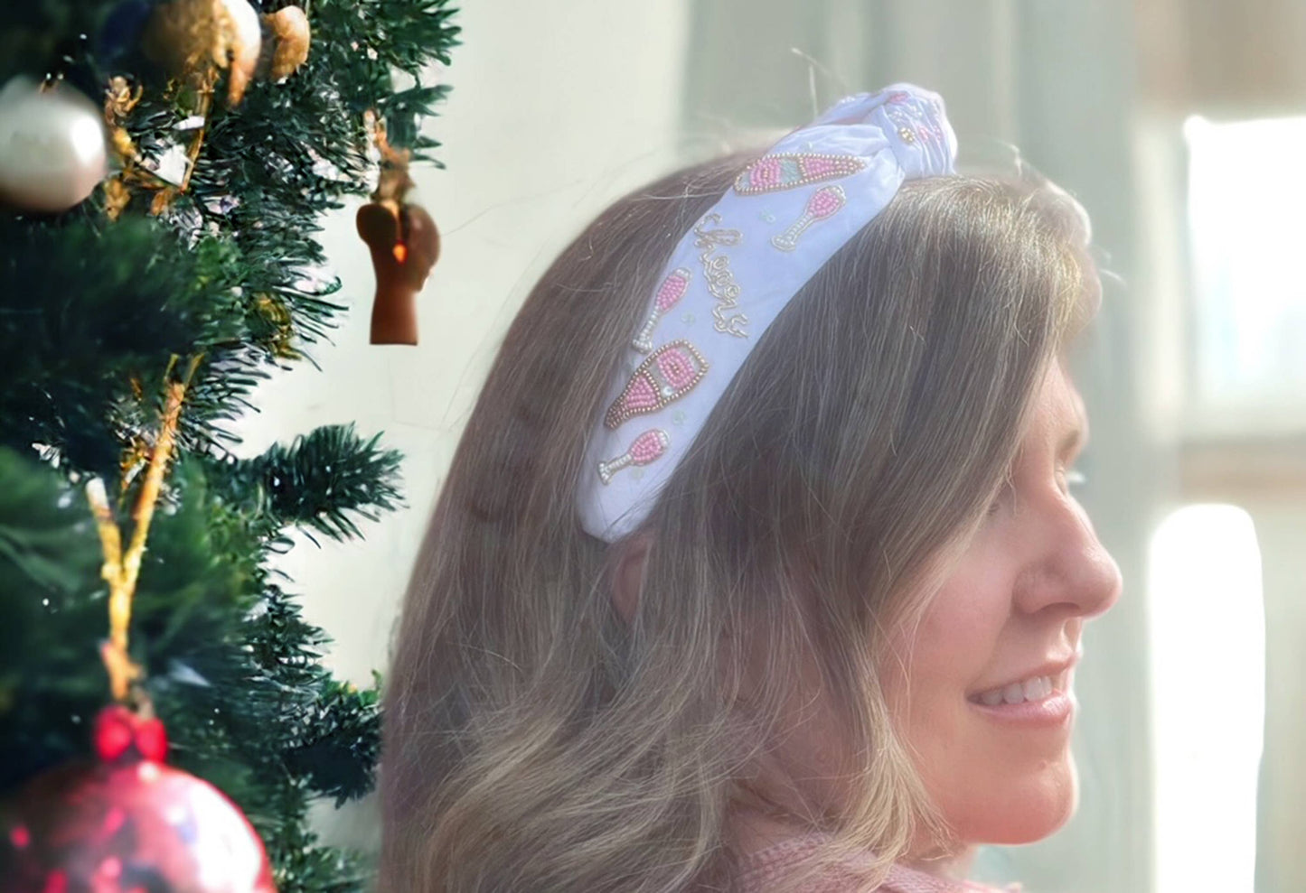 A woman wearing a Bash Beaded Pink Christmas Lights Headband in front of a Christmas tree.