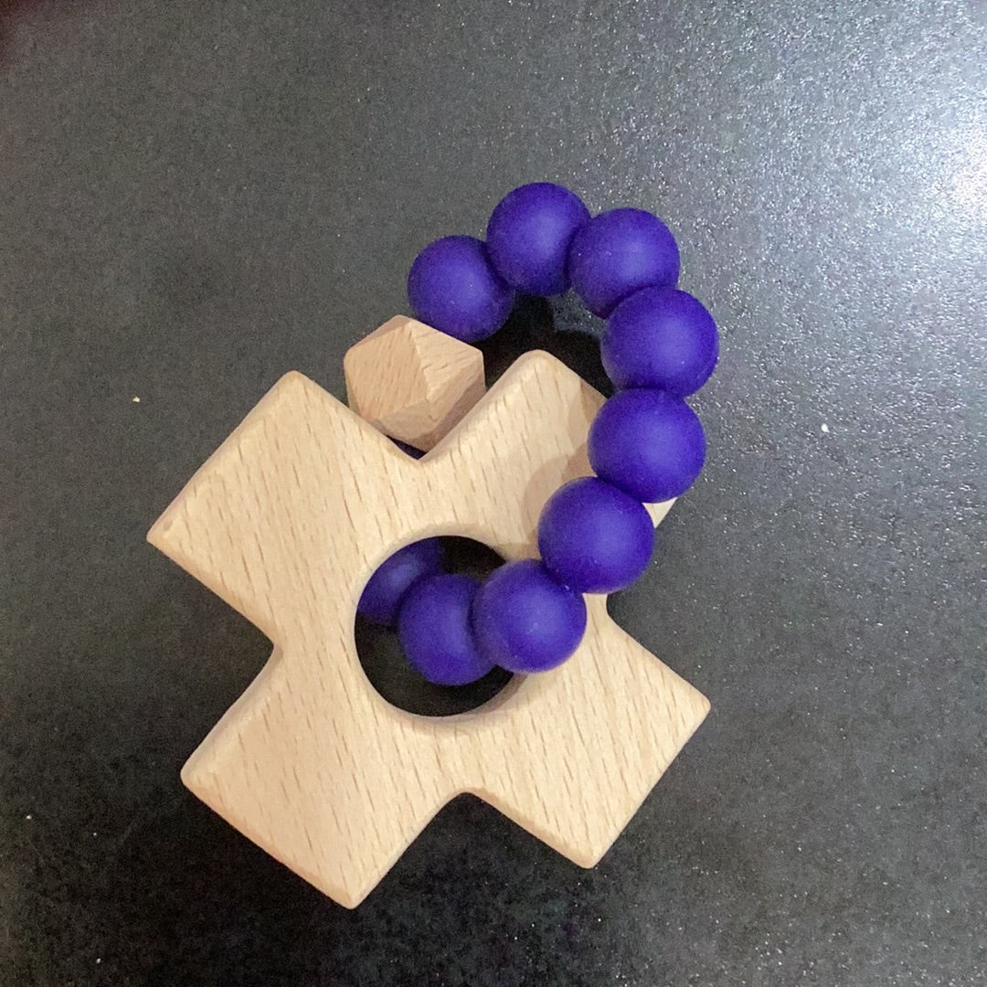 A Cross Teether by Chickie Collective with a purple bead on it.