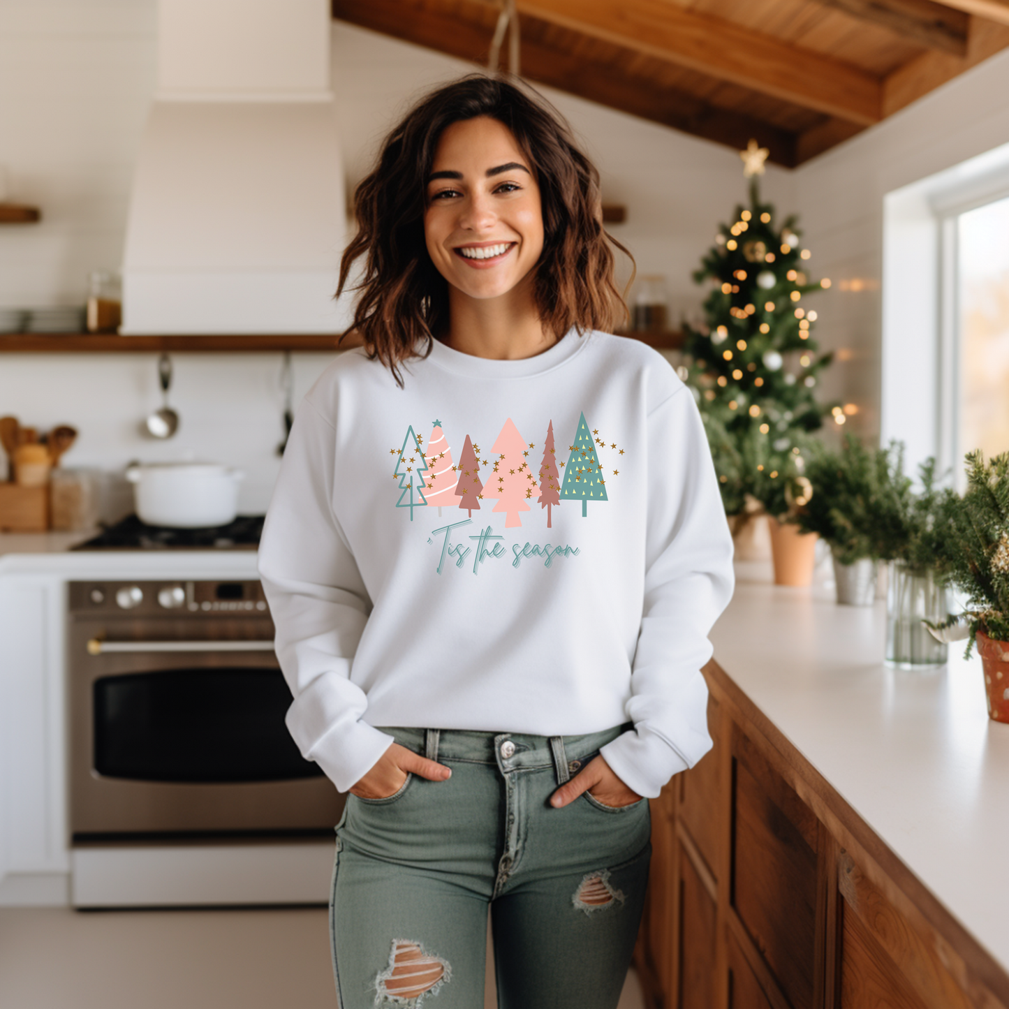 A cozy woman in a kitchen wearing a Printify White Christmas Tree Sweatshirt.