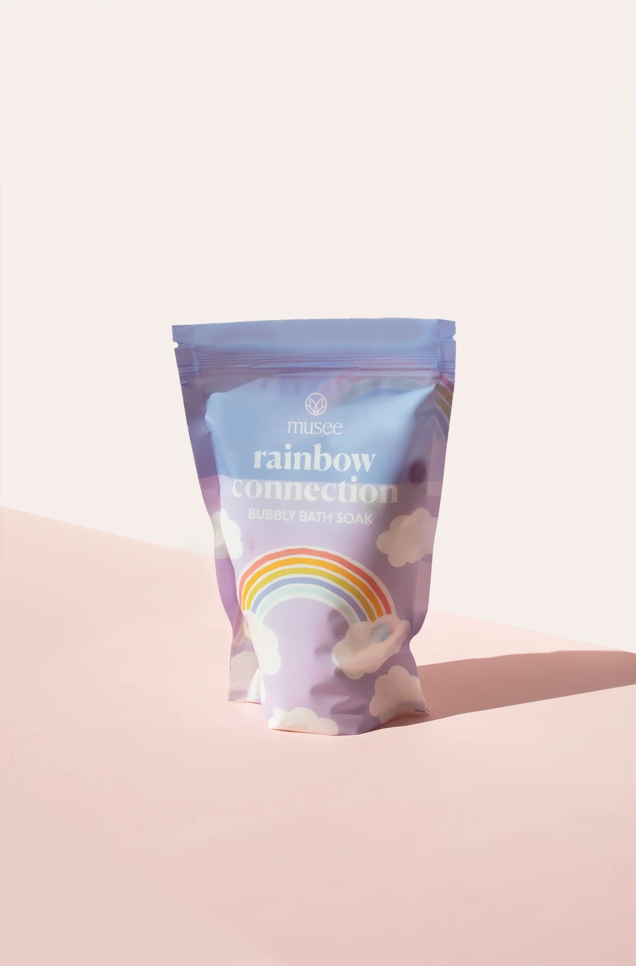 A bag of Rainbow Connection Bubbly Bath Soak by Musee on a vibrant pink background creates a magical oasis.