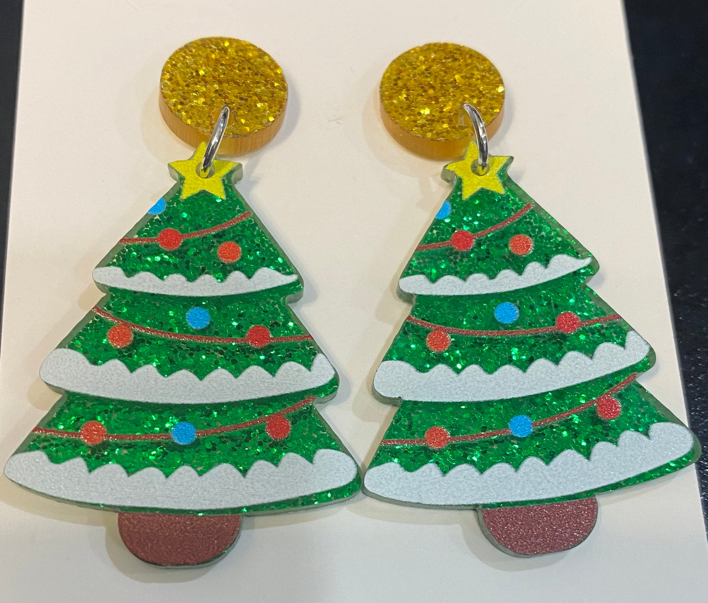 A pair of Festive Acrylic Christmas Tree Earrings by faire with glitter on them.