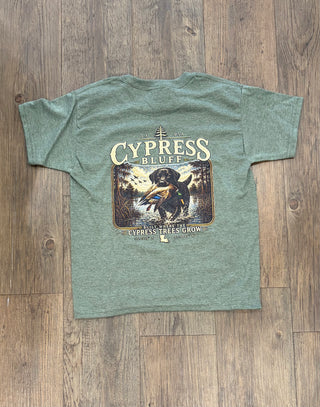 Sage green Cypress Bluff Kids Shirts Casual Everyday Tops for Boys and Girls featuring a back graphic of a Labrador retriever with a duck in a swamp, with text reading “Cypress Bluff” and “Built Where the Cypress Trees Grow.”.
