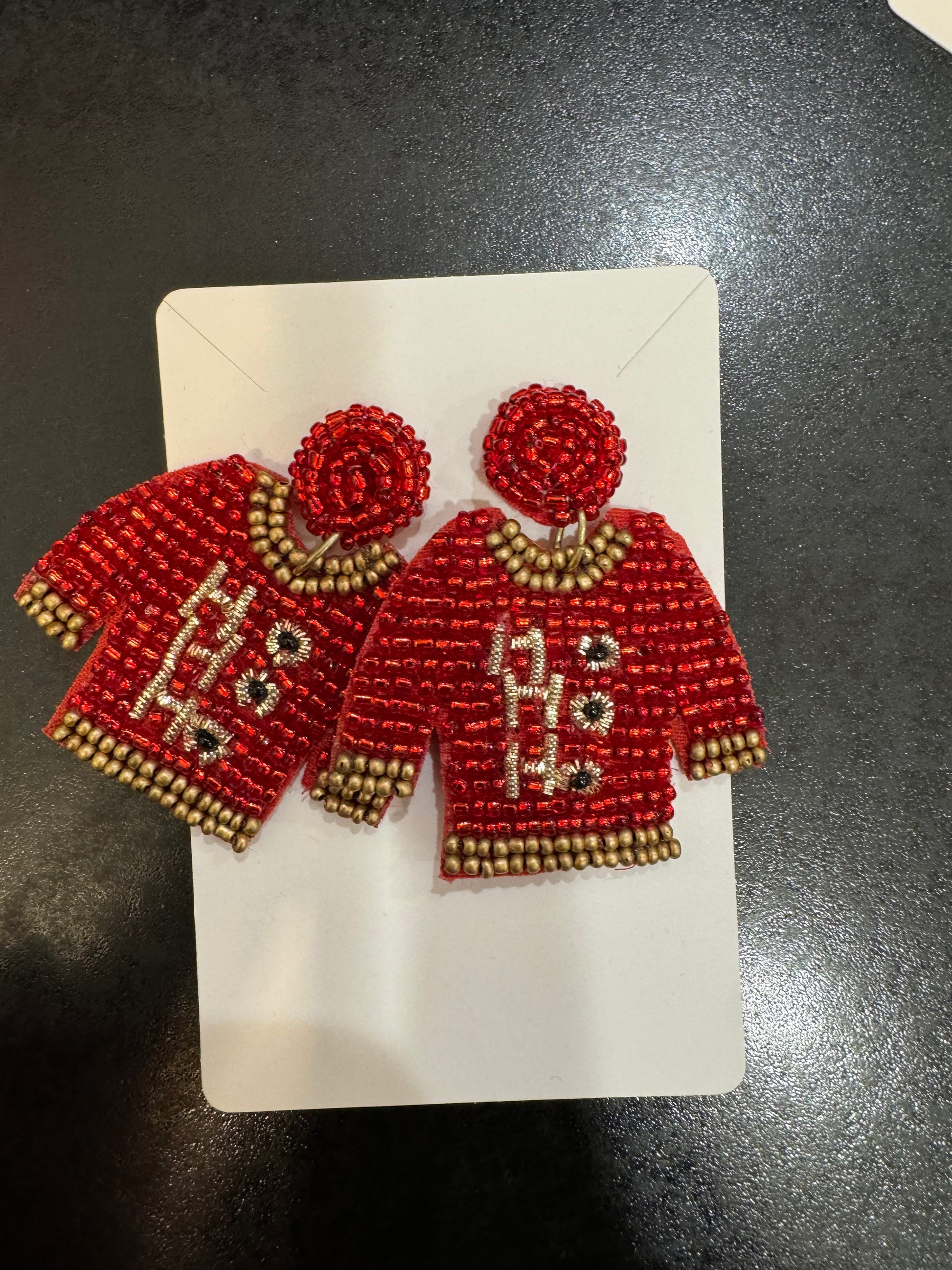 A pair of Chickie Collective Beaded Ho Ho Ho Sweater Earrings on a white piece of paper.