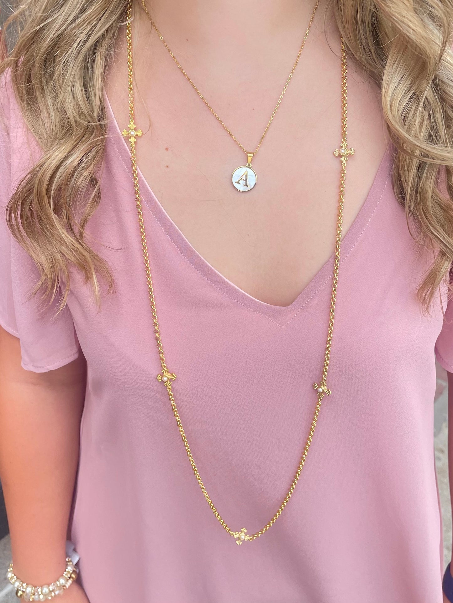 A woman wearing a pink shirt and a gold Weisinger Designs Long Necklace with Pearl Cross Connector.