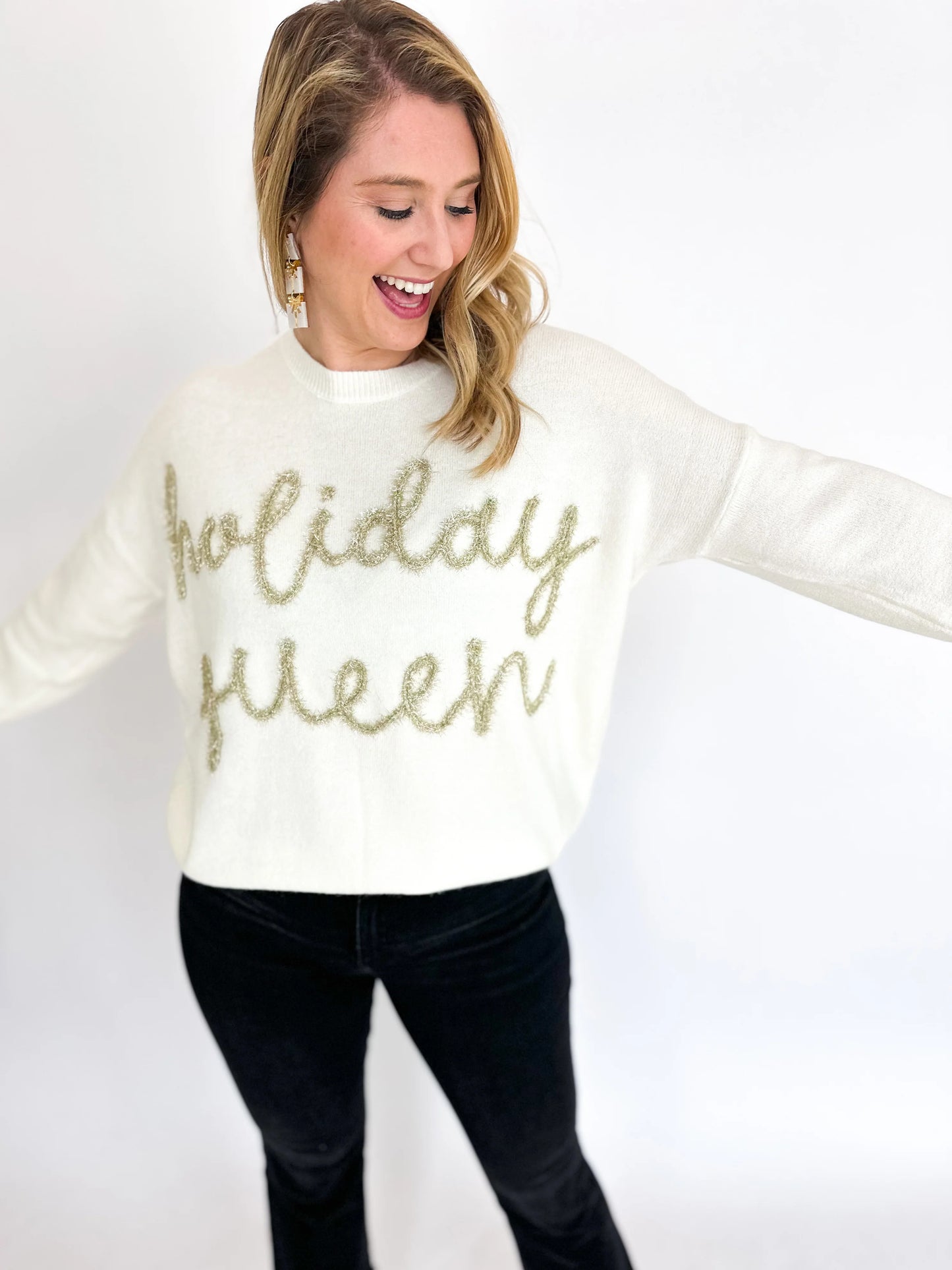 A cozy and stylish woman wearing a Gilli Holiday Queen Gold Tinsel Cream Sweatshirt.