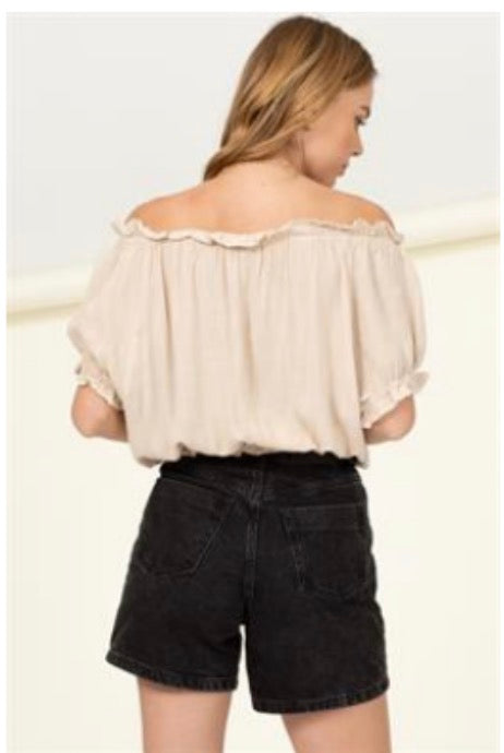The back view of a woman wearing black shorts and a HYFVE off the shoulder crop with gathered waist in Sand.