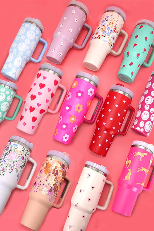 A group of colorful Wall To Wall Accessories 40oz STAINLESS STEEL TUMBLER mugs on a pink background.