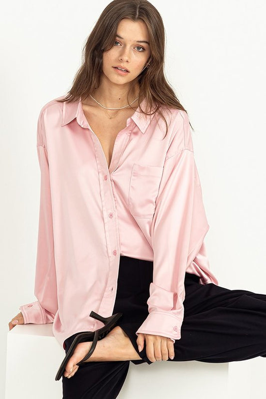 The model is wearing the HYFVE Completely Charmed Oversized Satin Shirt in pink and black pants.