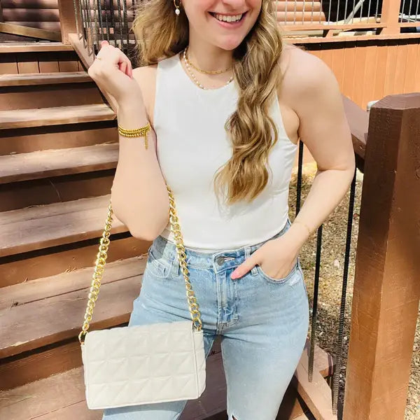 a woman wearing a white tank top and ripped jeans holding a Kaydee Lynn Aria Crossbody - Cream purse.