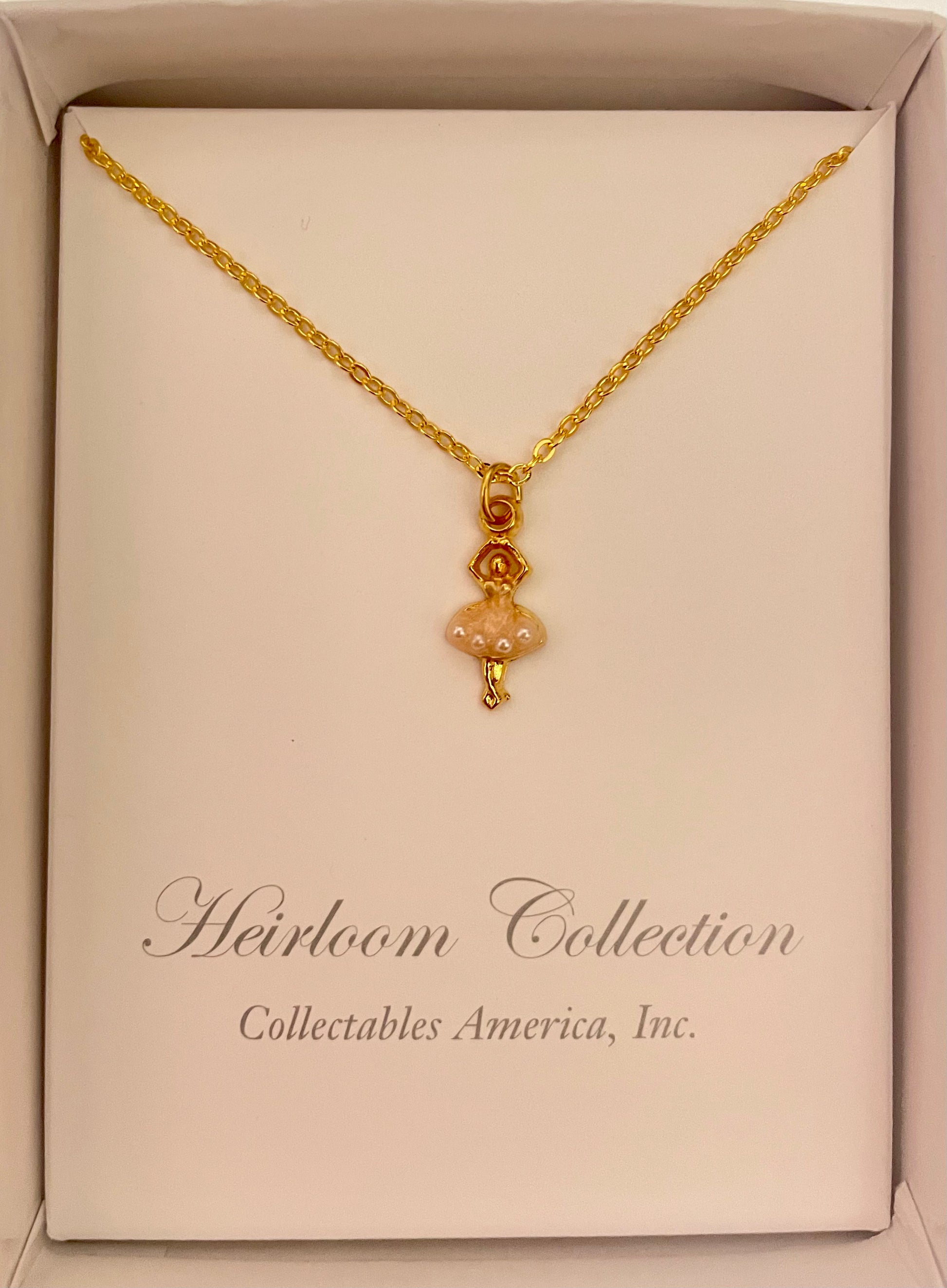 A Collectables America Gold Ballerina Necklace in a box on a table.