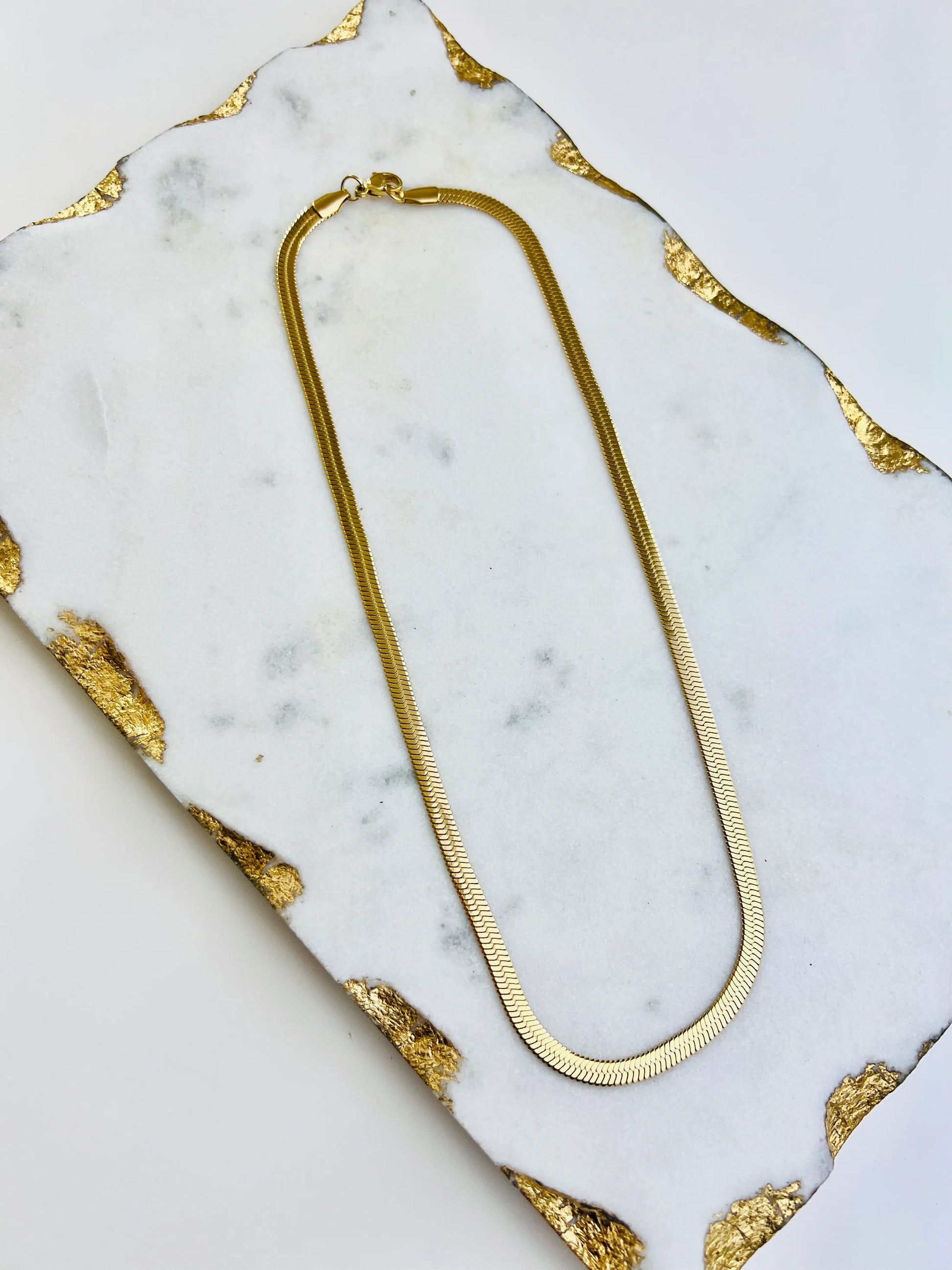 a Nicole Snake Necklace by Lacy Rae Jewelry on a marble surface.