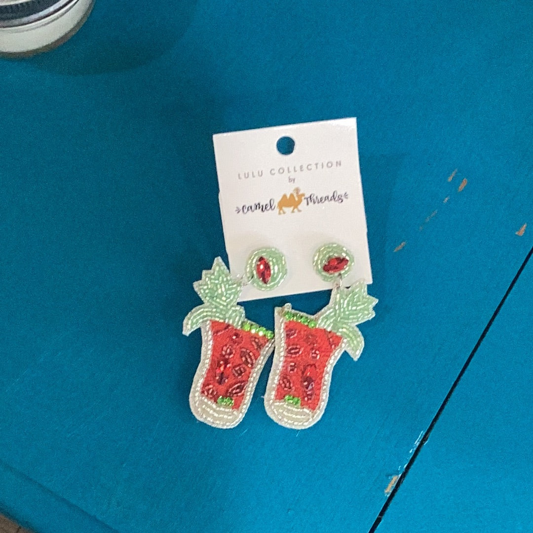 A pair of Beaded Earrings - Bloody Mary by Camel Threads on a blue table.
