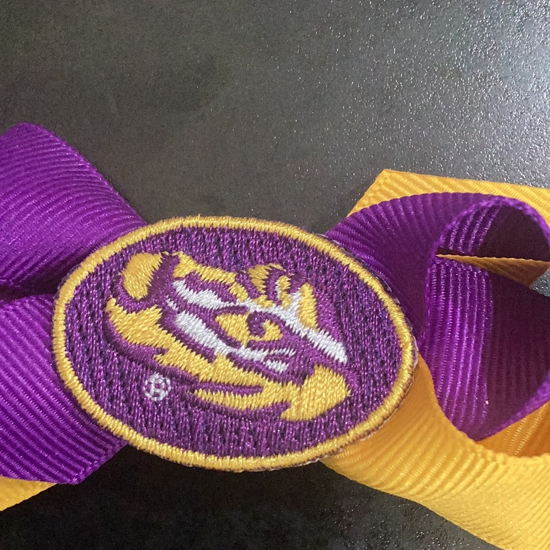 A mini purple Wee Ones LSU bow with embroidered eye of the tiger and a no-slip clip.