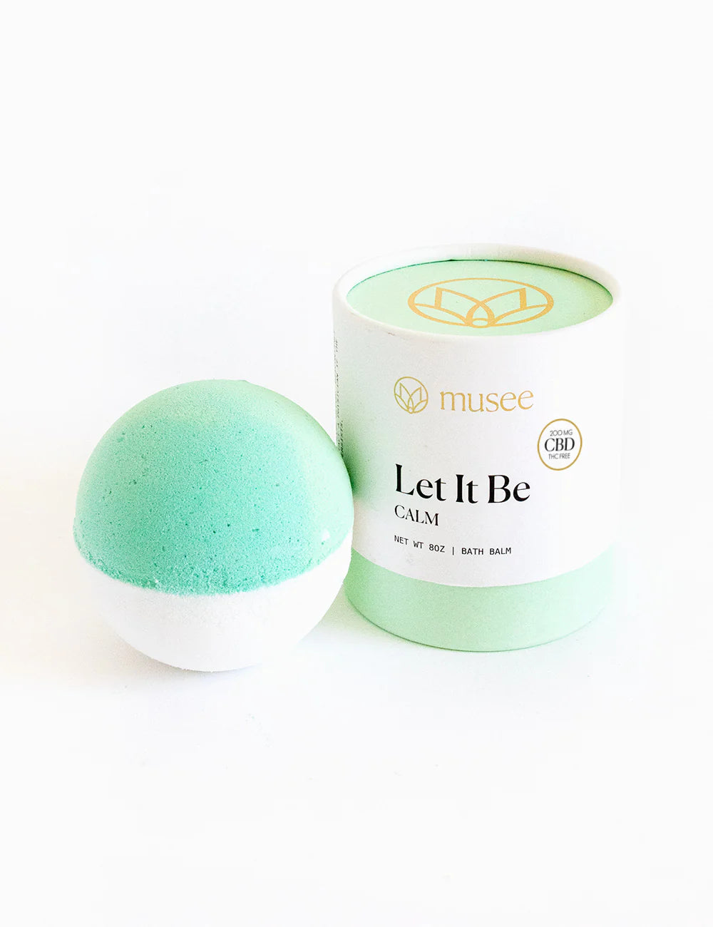 A Musee Let It Be Bath Balm in green and white next to a white container.