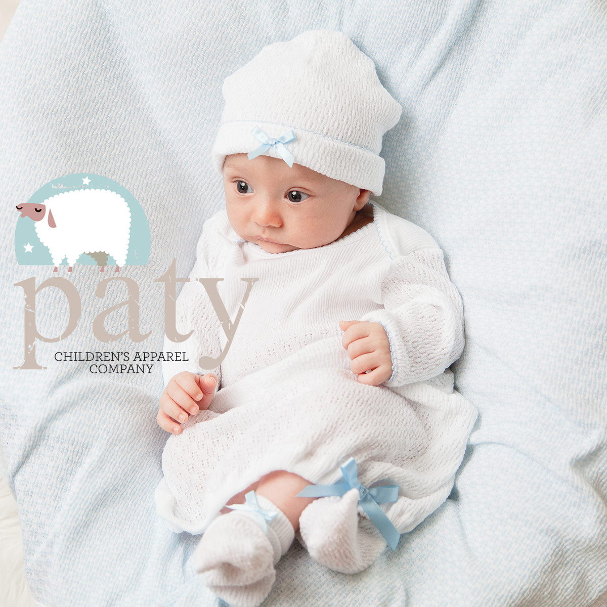 A baby is laying on a blue blanket with a Paty Signature Paty Gown.